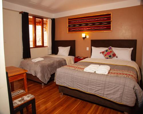 ein Hotelzimmer mit zwei Betten und einem Tisch in der Unterkunft El Chasqui in Ollantaytambo