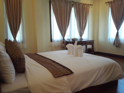 um quarto com uma cama com lençóis brancos e janelas em Baan Bussaba Hotel em Trang