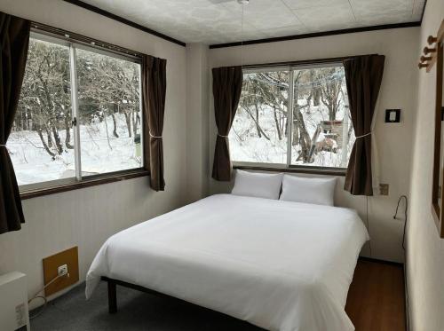 a bedroom with a white bed and two windows at Kamoshika Lodge Hakuba in Minami Otari