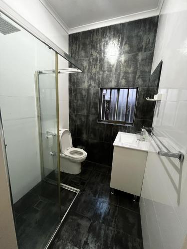 a bathroom with a toilet and a glass shower at Relaxed Cosy Beach Room Close to Airport in Sydney