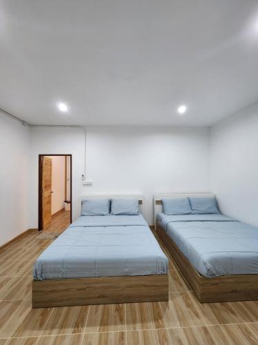 two beds in a room with white walls and wooden floors at 198 House in Ban Khlong Pleo