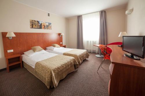 a hotel room with two beds and a desk and a television at Hotel Major Budget in Kraków