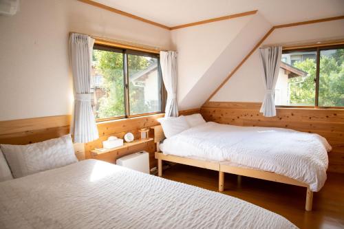 a bedroom with two beds and a chair and windows at 日田天ヶ瀬の源泉掛け流し温泉付き貸別荘 5名様まで同料金 in Hita