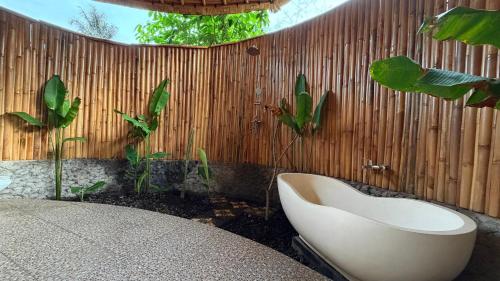 a bathroom with a white bath tub next to a wooden fence at Wana Bamboo House by ecobreeze in Sidemen