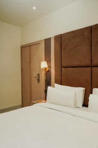 a bedroom with a large white bed with a wooden headboard at Hotel The Elite in Jabalpur