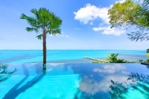 a swimming pool with a palm tree and the ocean at The Headland Villa 2, Samui in Koh Samui