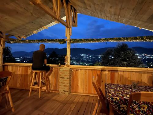 a man sitting on a stool on a deck looking out at night at Aika Sunrise - Your Home in the Hills in Iringa