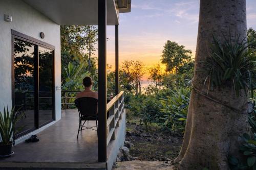 a person sitting in a chair on a porch watching the sunset at Sleep Inn - Lonely Beach in Ko Chang