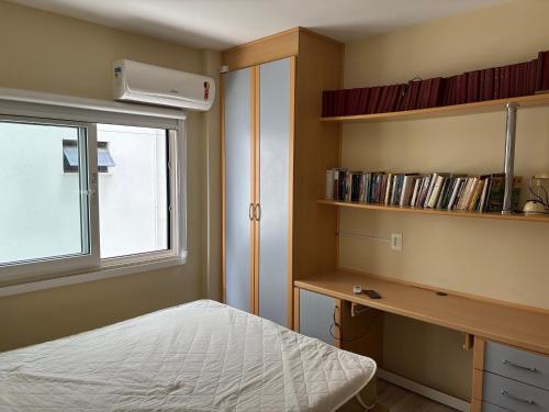 a bedroom with a bed and a desk and a window at Vista para o molhe in Itapema
