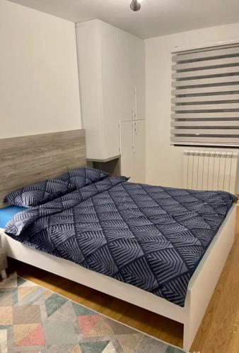a bedroom with a bed with a blue comforter and a window at Apartman Hilandarska in Lukavica