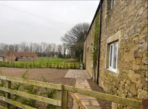 a stone building with a fence next to it at Beautiful Countryside Cottage Alnwick Northumberland in Alnwick