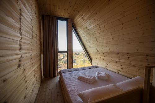 a bed in a wooden room with a large window at Kvirike Hills Cottages in K'obulet'i