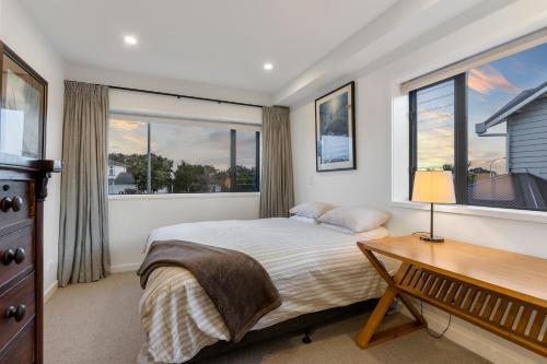 a bedroom with a bed and a desk and windows at Stylish Townhouse in Auckland