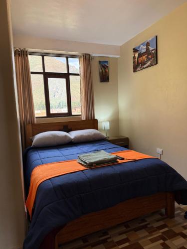 a bedroom with a bed with an orange blanket and a window at Hospedaje el Indi0 in Pisac
