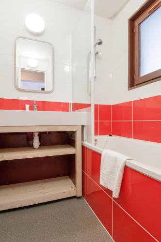 La salle de bains rouge et blanche est pourvue d'un lavabo et d'une baignoire. dans l'établissement Residence Antares - maeva Home, à Avoriaz