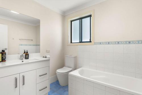a bathroom with a tub and a toilet and a window at White Sands Villa by Experience Jervis Bay in Huskisson