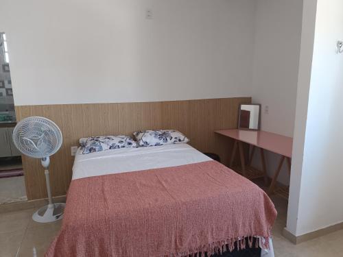 a bedroom with a bed and a desk and a fan at Kitnet amplo in Santa Cruz Cabrália