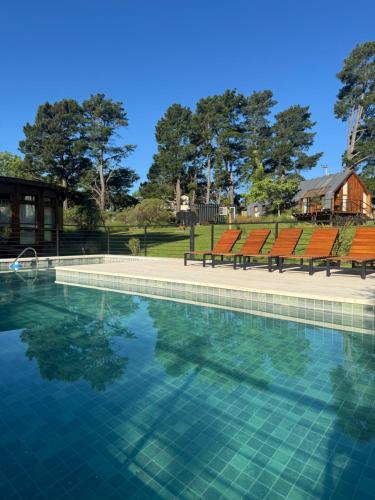 a swimming pool with orange chairs and a house at Cabañas Punto Prana in Tandil