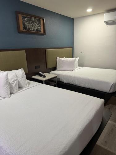 two beds in a hotel room with white sheets at DTLV, a Baymont by Wyndham in Las Vegas