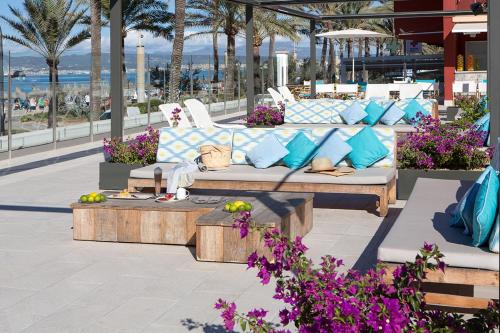a patio with a couch and tables and palm trees at Universal Hotel Neptuno - Adults Only in Playa de Palma