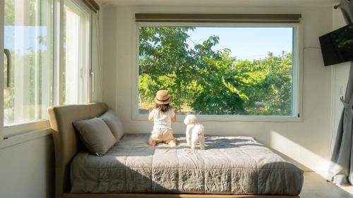 a little girl sitting on a bed looking out the window at Yangyang Slowstay Pension in Yangyang