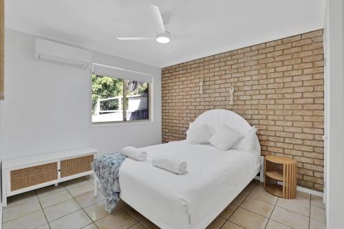 a white bed in a room with a brick wall at Barefoot Haven in Amity Point