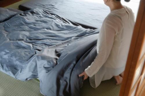 a woman is standing next to a bed at 島原の一棟貸し まちの宿山と朝 in Shimabara