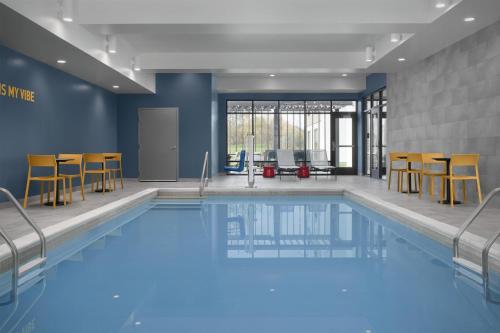 a swimming pool with chairs and a table in a building at Home2 Suites By Hilton Syracuse Liverpool Airport Area in Liverpool
