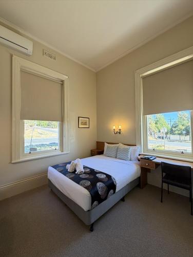 a bedroom with a bed and a desk and two windows at Campbell st Lodge in Castlemaine