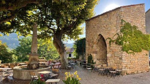 un edificio in pietra con tavoli, sedie e un albero di Chambre indépendante maison Typique Provençale a Seillans