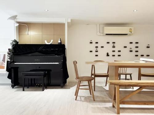 a black piano in a room with a table and chairs at Baan Rak BTS phromphong Emsphere in Bangkok
