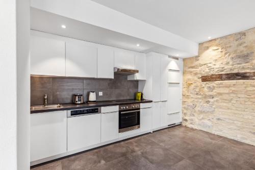 a kitchen with white cabinets and a stone wall at The R Apartment Rosengasse in Schaffhausen