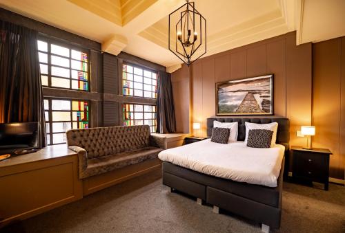 a bedroom with a bed and a couch and a chandelier at Hotel Huis van Bewaring - Bijzonder boutique hotel in historisch pand in Almelo