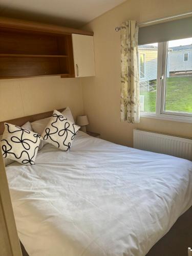 a white bed with two pillows and a window at Relax By The Coast - Spacious 6-sleeper Caravan in Leysdown-on-Sea