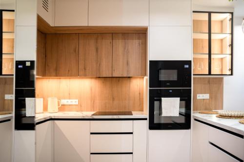 a kitchen with white cabinets and black appliances at Apartament Zakrzówek - Chilloway in Krakow