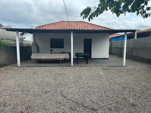 una piccola casa bianca con una panchina e un tavolo di Bela casa de praia a Palhoça