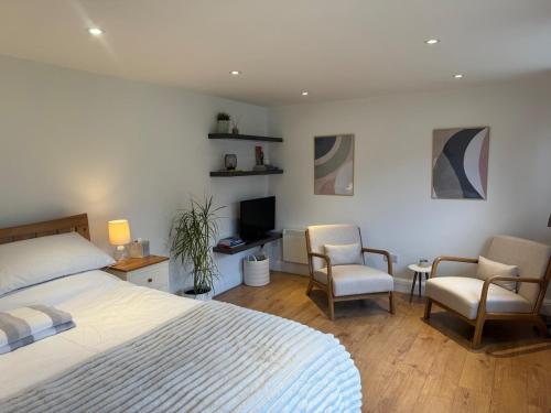 a bedroom with a bed and two chairs and a television at Cosy cabin nestled in the Surrey Hills in Dorking