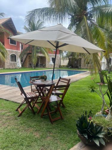 a table and chairs under an umbrella next to a pool at Chalé em Condomínio com in Aracati