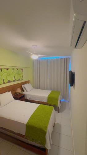 two beds in a hotel room with a green blanket at Enseada Praia do Forte in Praia do Forte