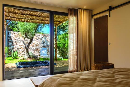 een slaapkamer met een grote glazen deur naar een patio bij Hôtel Les Suites Du Maquis in Bonifacio