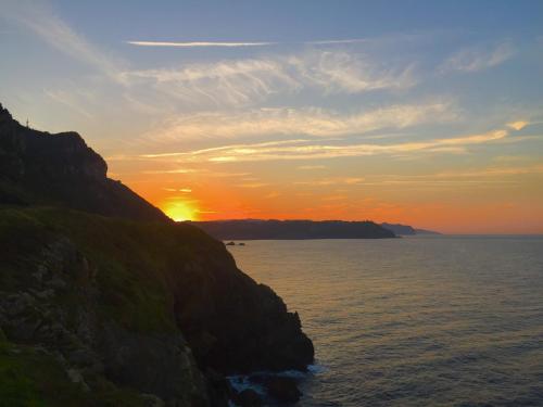 a sunset over the ocean next to a cliff at Lekeitio Aterpetxea Hostel in Lekeitio