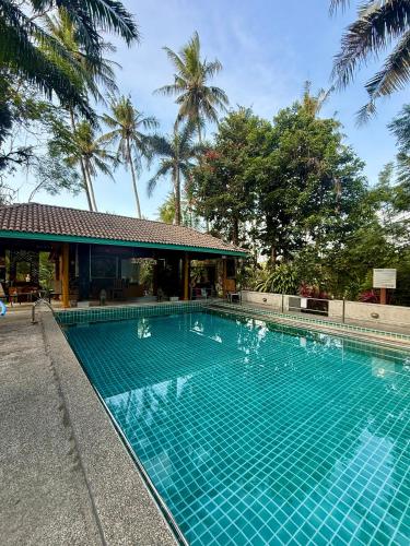 a blue swimming pool with palm trees in the background at Baan Rim Tarn B&B in Takua Pa
