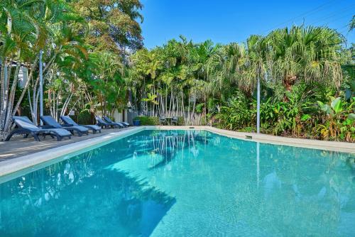 a swimming pool with chairs and palm trees at Trinity Beach Club Holiday Apartments in Trinity Beach