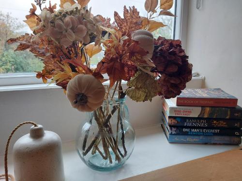 a vase with flowers in it on a table with books at Sett Cottage, Hayfield in Hayfield