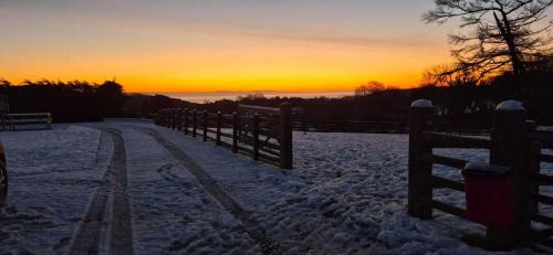 a fence in the snow with a sunset in the background at Evening Star Cottages in Saundersfoot