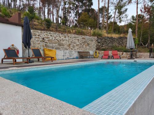 a swimming pool with chairs and umbrellas next to a wall at Casa do Reguengo, Freigil in Resende