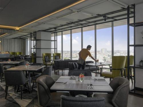 泗水Movenpick Surabaya City的一名男子站在摆着桌椅的餐厅里