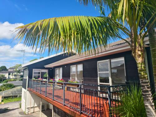 a house with a balcony and a palm tree at Sweet North Cote Stay in Auckland