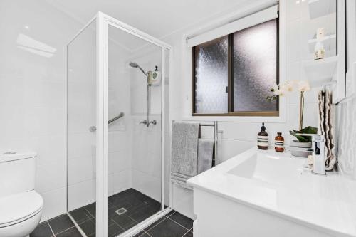 a white bathroom with a shower and a toilet at Mollymook Den Coastal Retreat - Walk to Beach & Town in Mollymook