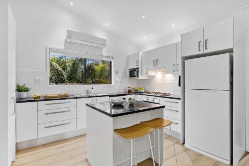 a kitchen with white cabinets and a white refrigerator at Mollymook Den Coastal Retreat - Walk to Beach & Town in Mollymook